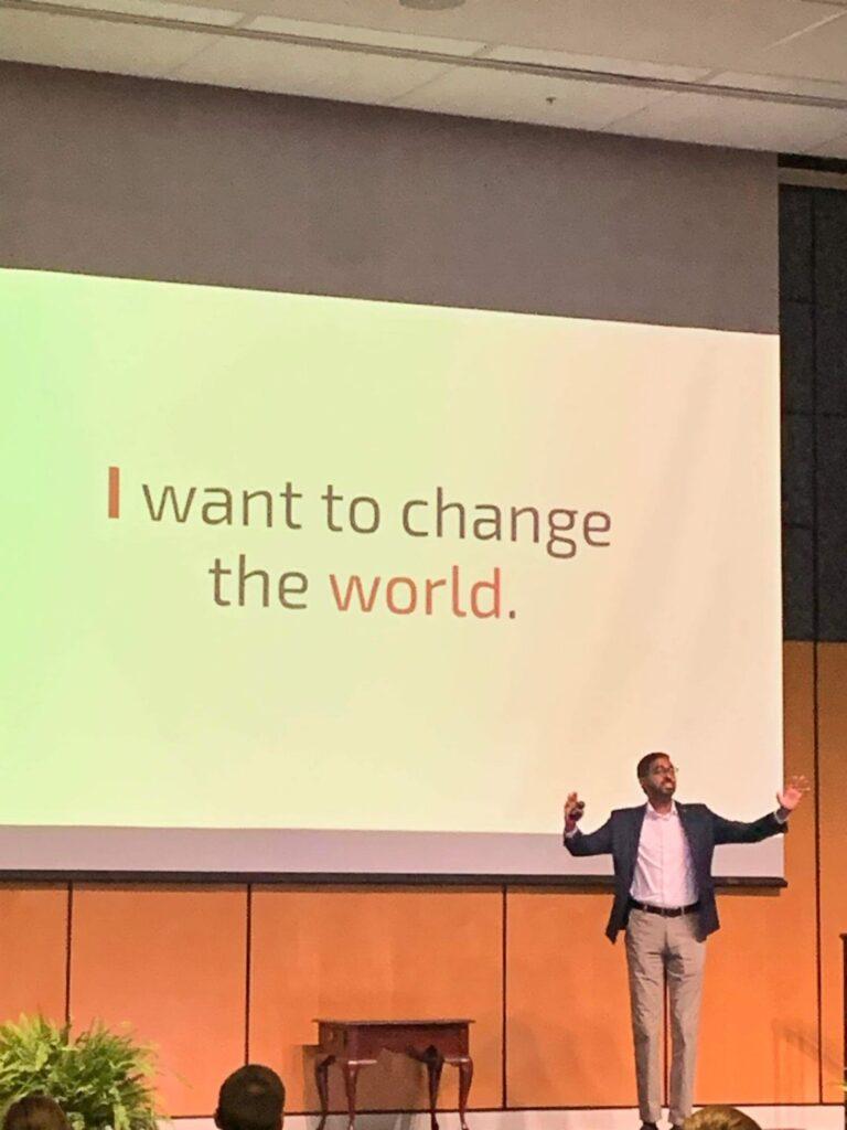 A picture of Nipuna Ambanpola speaking to the audience. The image on the screen says "I want to change the world" in big letters.